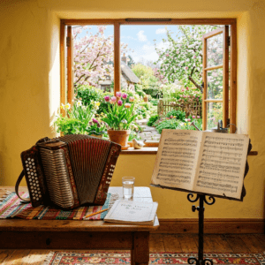 Accordion on table with sheet music stand by open window showing colorful garden
