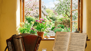 Accordion on table with sheet music stand by open window showing colorful garden